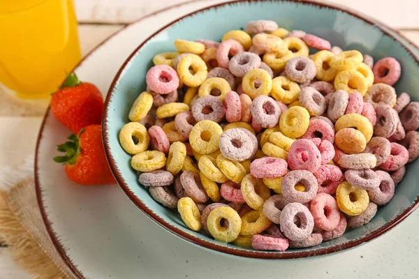 Bowl of colorful cereal rings and strawberries on white wooden background