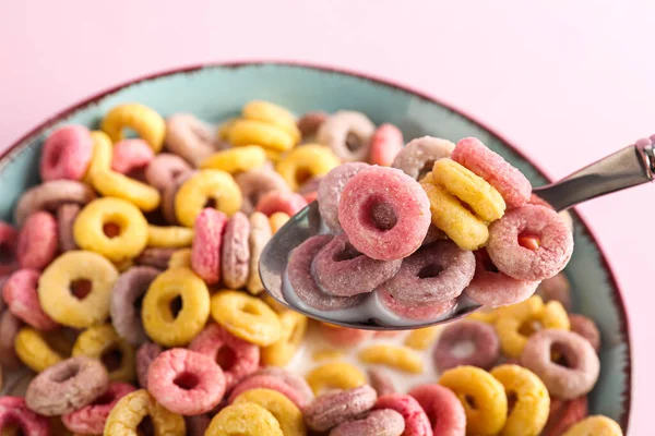 Bowl and spoon of colorful cereal rings with milk on pink background