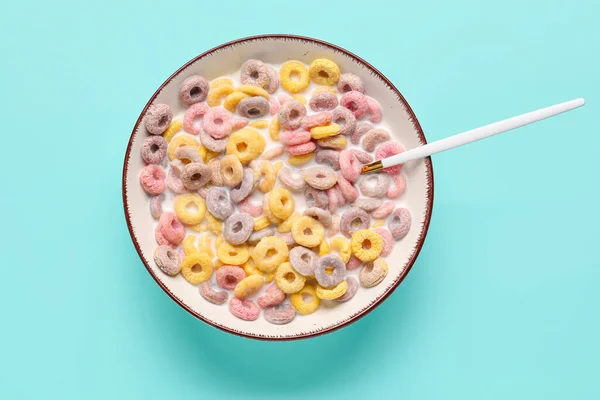 Bowl and spoon of colorful cereal rings with milk on turquoise background