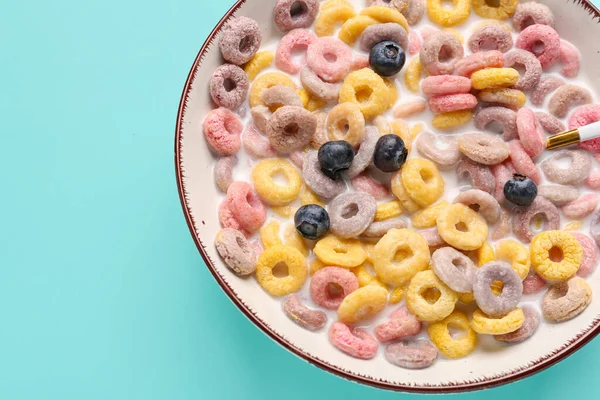 Bowl of colorful cereal rings with milk and blueberries on turquoise background