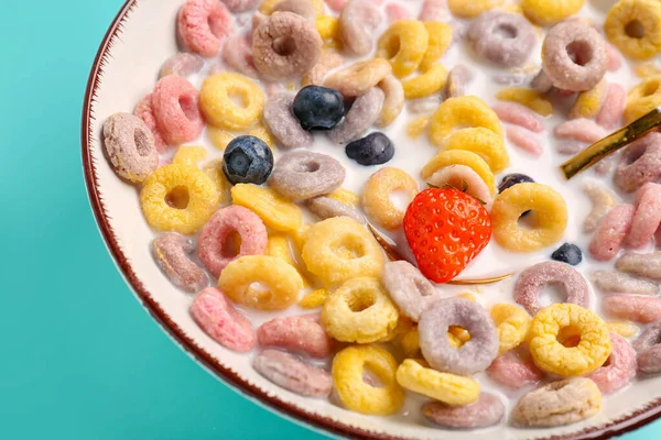 Bowl of colorful cereal rings with milk, strawberry and blueberries on turquoise background