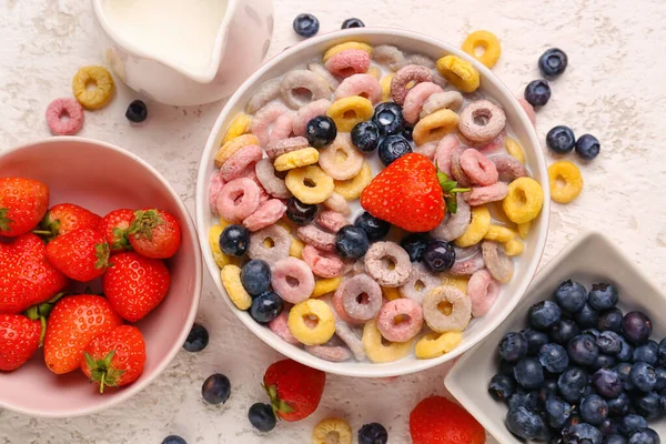 Bowl of colorful cereal rings with milk and berries on white grunge background