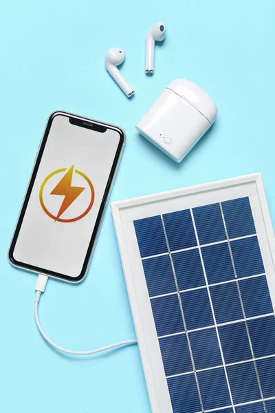 Portable solar panel with mobile phone and earphones on blue background