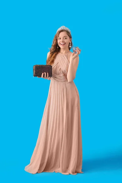 Young woman in prom dress with purse and perfume on blue background