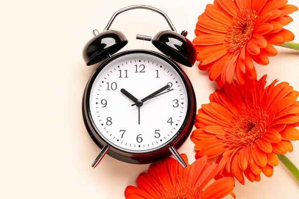 目覚まし時計と美しいガーベラの花のベージュの背景 — ストック写真