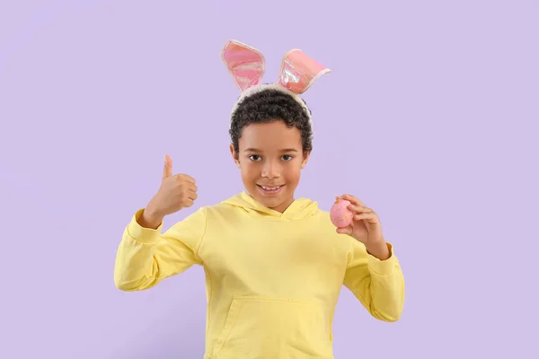アフリカ系アメリカ人の男の子でウサギ耳でイースターエッグショー親指アップ上ライラック背景 — ストック写真