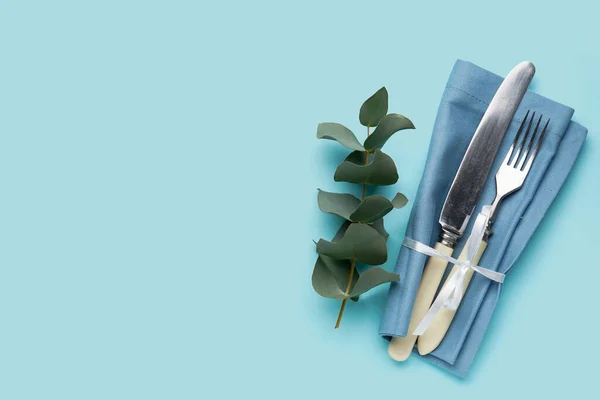 Set of cutlery in napkin and eucalyptus branch on blue background
