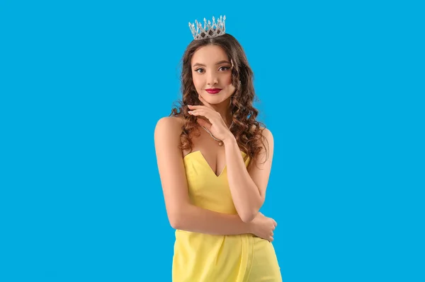 Beautiful young woman in prom dress and tiara on blue background
