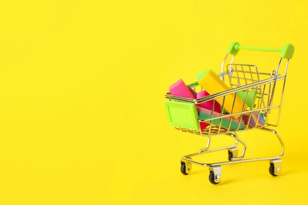 Shopping cart with erasers and chalk on yellow background