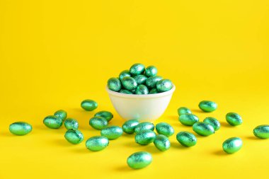 Sarı arka planda renkli folyoyla bir kase çikolatalı Paskalya yumurtası.