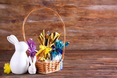 Çikolatalı sepet Paskalya yumurtası ve seramik tavşanlar ahşap masada.