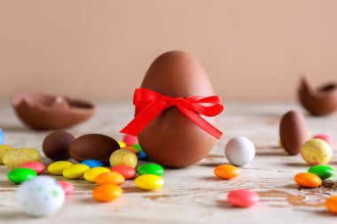 Çikolatalı Paskalya yumurtası ve şeker, kahverengi arka planda, ahşap masada.
