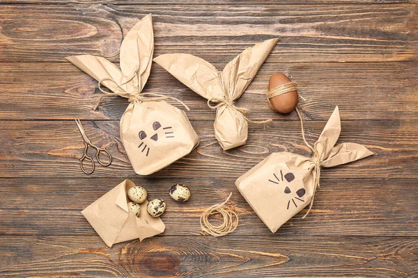 stock image Composition with bunny gift bags, Easter eggs, scissors and thread on brown wooden background