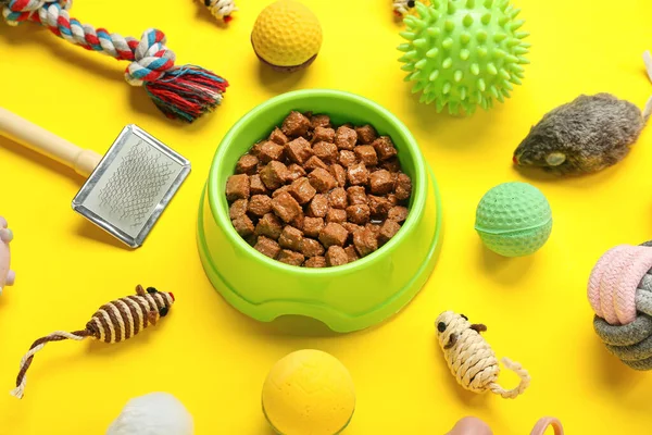 Composition with different pet care accessories and wet food on yellow background