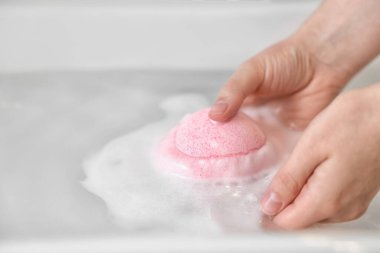Kadın evdeki suya pembe banyo bombası koyuyor, yakın plan.