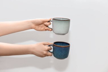 Gri arka planda farklı bardaklar tutan kadın