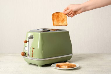 Beyaz masada, modern ekmek kızartma makinesinden çıtır ekmek dilimi alan bir kadın.