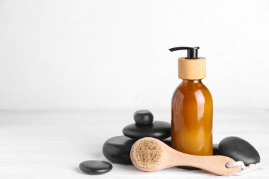 Massage brush, bottle of cosmetic product and spa stones on light wooden table