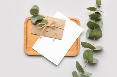 Beyaz arkaplanda boş kart, zarf ve okaliptüs dalları içeren kompozisyon