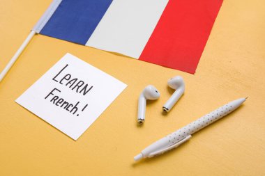 Sarı arka planda Learn FRENCH, kulaklıklar, Fransa 'nın kalem ve bayrağı yazılı kağıt, yakın plan