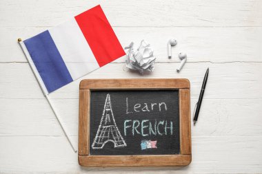 Beyaz ahşap zemin üzerinde LEARN FRENCH, bayrak, buruşuk kağıt ve kulaklık yazılı kamış tahtası