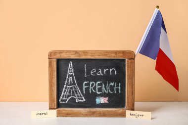 Tebeşir tahtası. Yazılı LEARN FRENCH, kelimeler ve bayrak bej duvarın yanındaki masada.