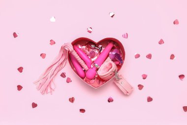 Seks oyuncaklarıyla hediye kutusu ve pembe arka planda konfeti.