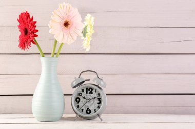 Ahşap zemin üzerinde güzel Gerbera çiçekleri olan çalar saat ve vazo.