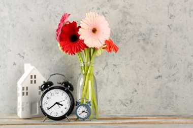 Gri grunge arka planında Gerbera çiçekleri olan çalar saatler ve vazo.