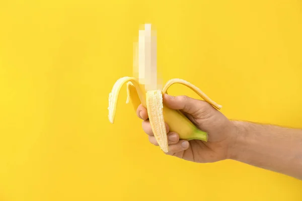 Male hand with banana on yellow background. Concept of sex education