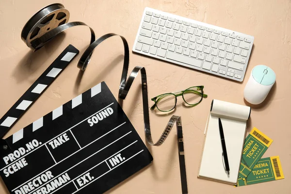 Movie clapper with reel, eyeglasses, computer keyboard, mouse and notebook on beige background