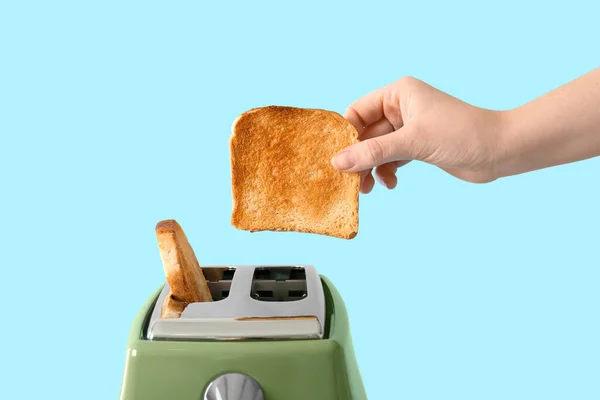 Frau Nimmt Knusprige Brotscheibe Aus Modernem Toaster Auf Blauem Hintergrund — Stockfoto