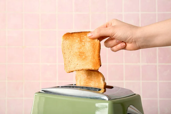 在粉红瓷砖背景下从现代烤面包机上取出脆面包片的女人 — 图库照片