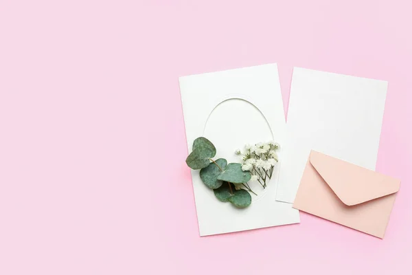 Composition with blank cards, envelope, gypsophila flowers and eucalyptus branch on pink background