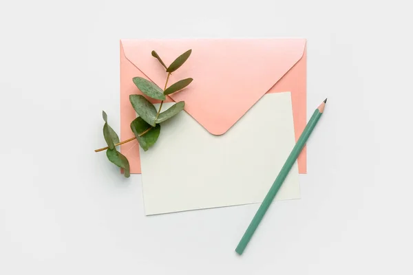 Blank card, envelope, pencil and eucalyptus branch on white background