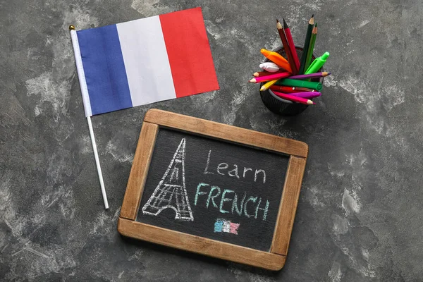 Chalkboard with text LEARN FRENCH, flag and pen cup on dark background