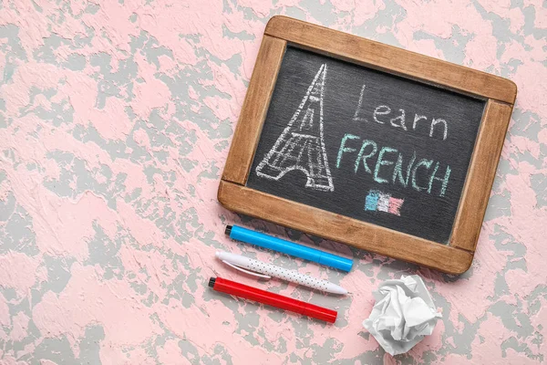 Chalkboard with text LEARN FRENCH, pens and crumpled paper on grunge background