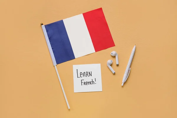 Paper with text LEARN FRENCH, earphones, pen and flag of France on yellow background