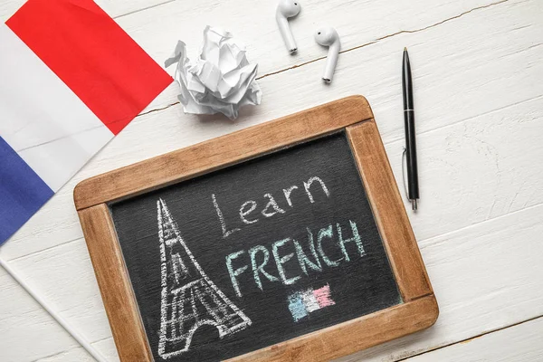 stock image Chalkboard with text LEARN FRENCH, flag, crumpled paper and earphones on white wooden background