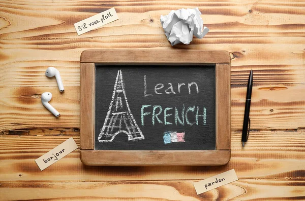 Chalkboard with text LEARN FRENCH, earphones, pen and crumpled paper on wooden background