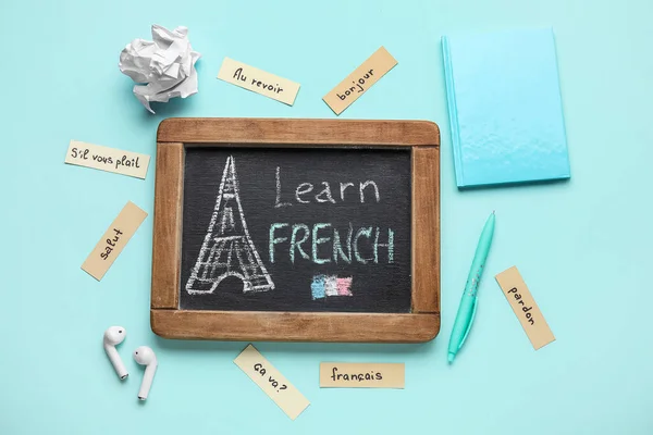 Chalkboard with text LEARN FRENCH, stationery and earphones on blue background