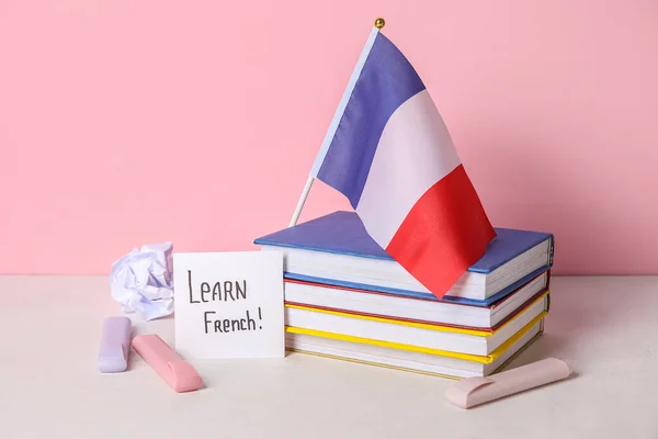 Paper with text LEARN FRENCH, pens, flag and books on table near pink wall