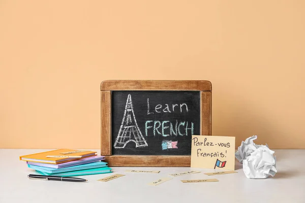 Chalkboard with text LEARN FRENCH and stationery on table near beige wall