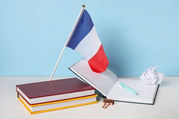 Flag of France with books and crumpled paper on table near blue wall