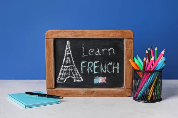 Chalkboard with text LEARN FRENCH and stationery on table near blue wall
