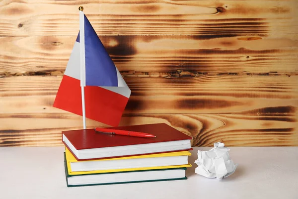 Flag of France with books and crumpled paper on table near wooden wall