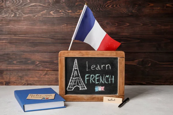 Koyu ahşap duvarın yanındaki masada Learn FRENCH, bayrak ve kitap yazılı kamış tahtası.