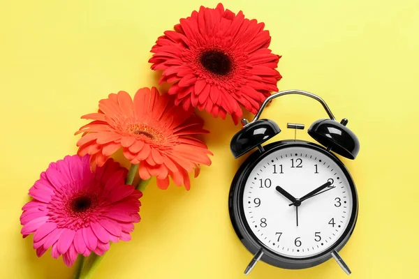 Väckarklocka Och Vackra Gerbera Blommor Gul Bakgrund — Stockfoto