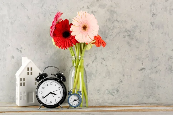 stock image Alarm clocks and vase with beautiful gerbera flowers on grey grunge background