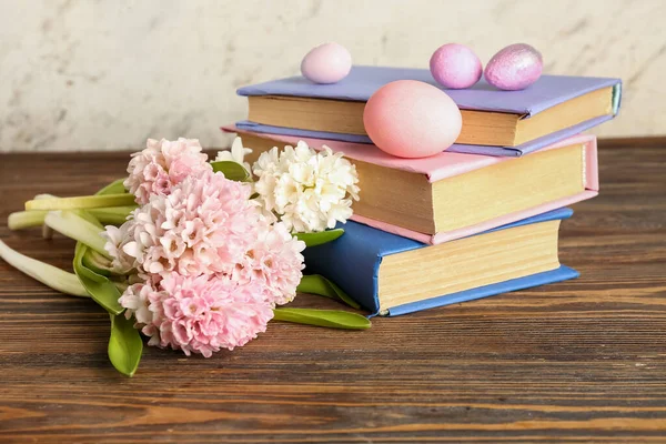 Beautiful hyacinth flowers, Easter eggs and books on wooden table near beige wall